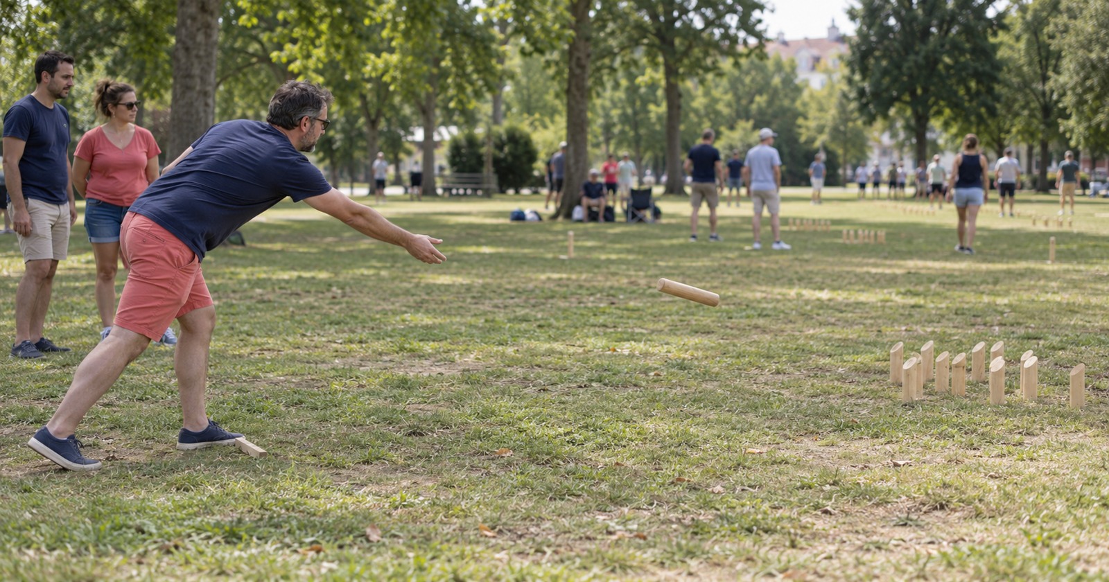 Un joueur lance un bâton vers des quilles de mölkky dans un parc, accompagné d’autres participants.